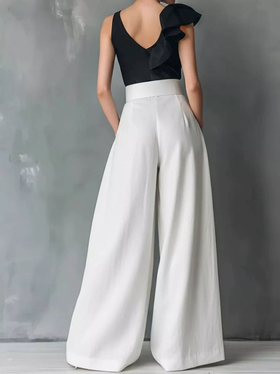 Person wearing a black top and white wide-leg pants against a gray background