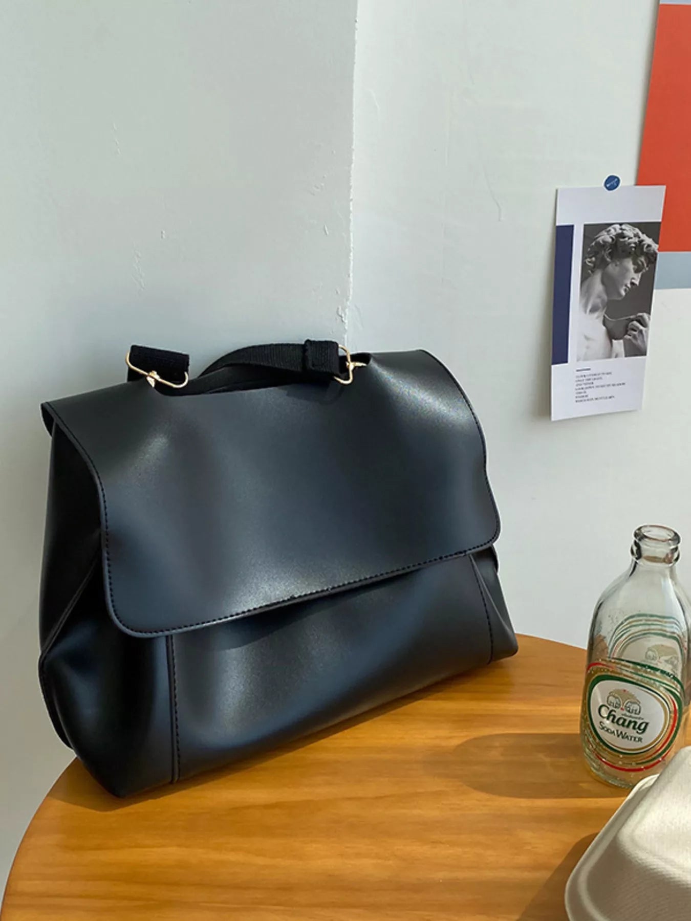 Black leather bag on a wooden surface with a bottle and photo in the background