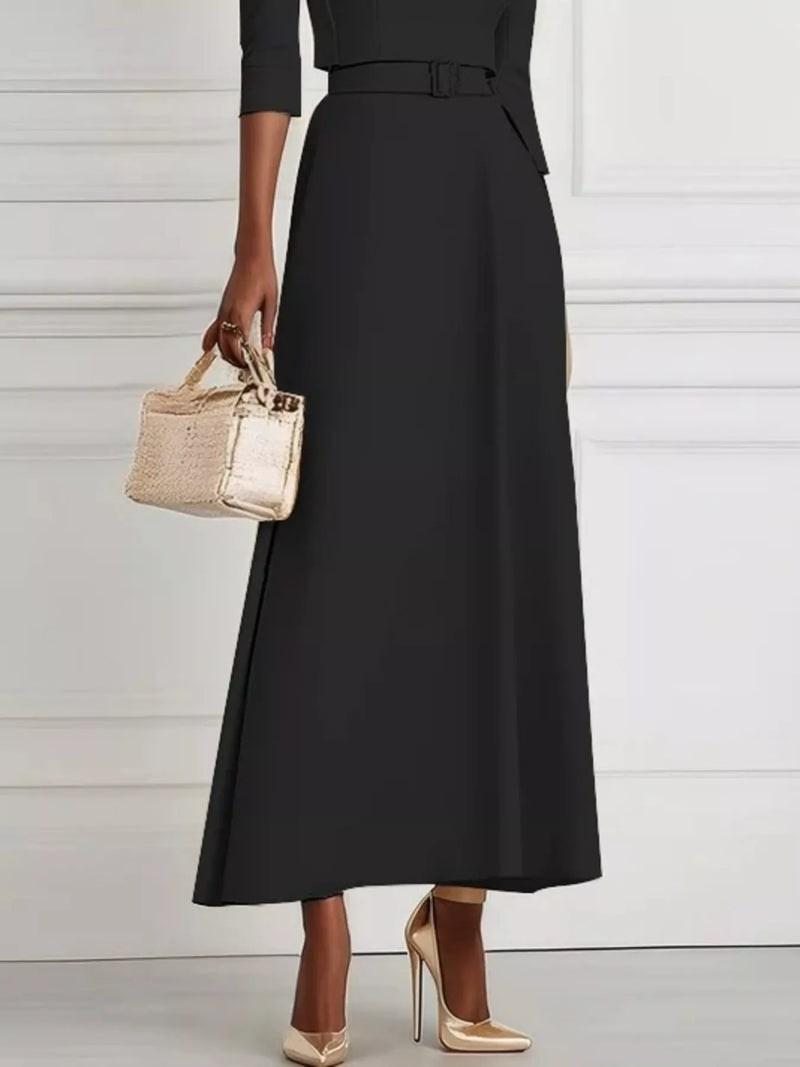 Person wearing a black dress holding a small gold handbag against a white background