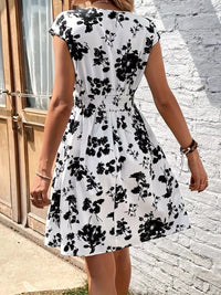 Woman wearing a black floral dress standing against a brick wall.