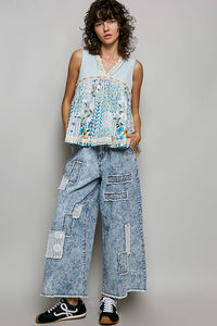 Woman wearing a sleeveless top with floral patterns and wide-leg jeans on a plain background