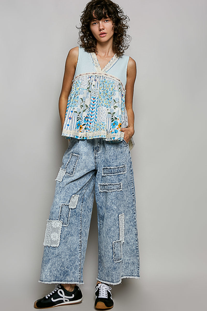 Woman wearing a sleeveless top with floral patterns and wide-leg jeans on a plain background
