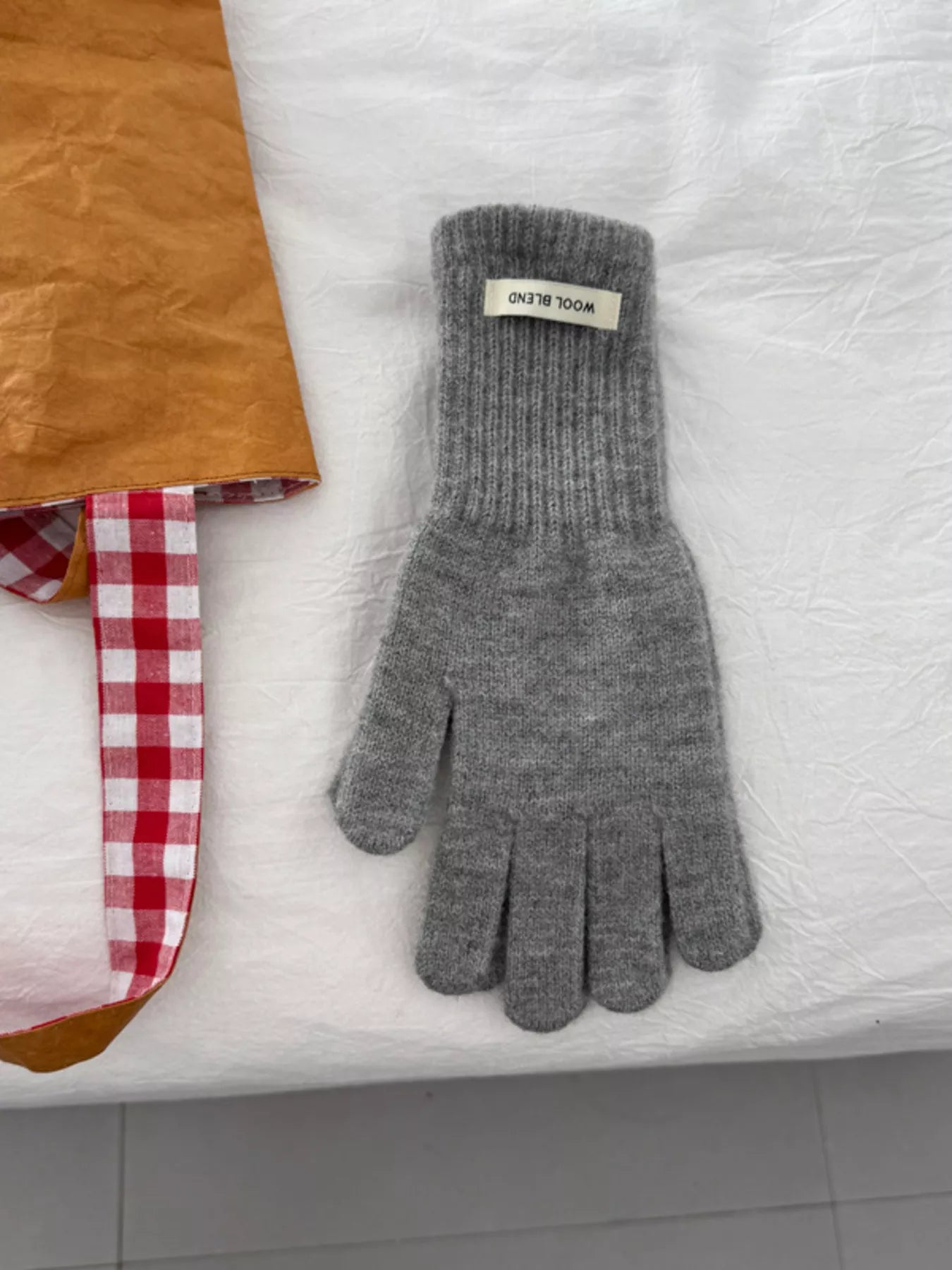 Gray knit glove on a white surface with a checkered cloth and brown paper bag in the background.