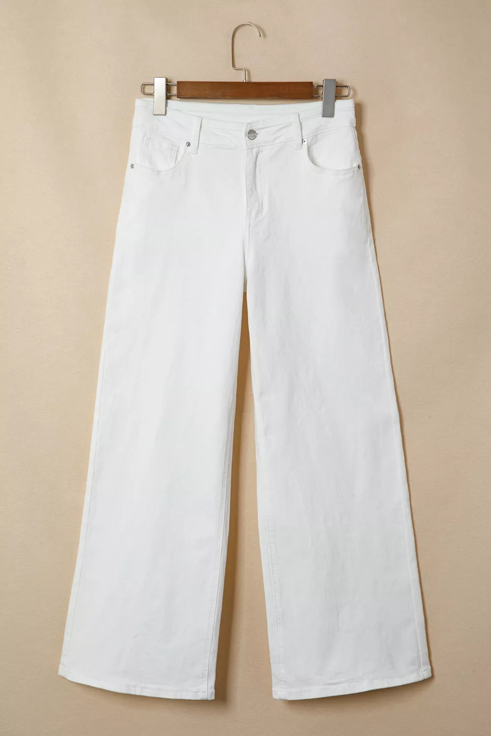 White wide-leg jeans hanging on a wooden hanger against a beige background