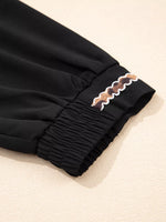 Black pants with decorative trim on a beige background
