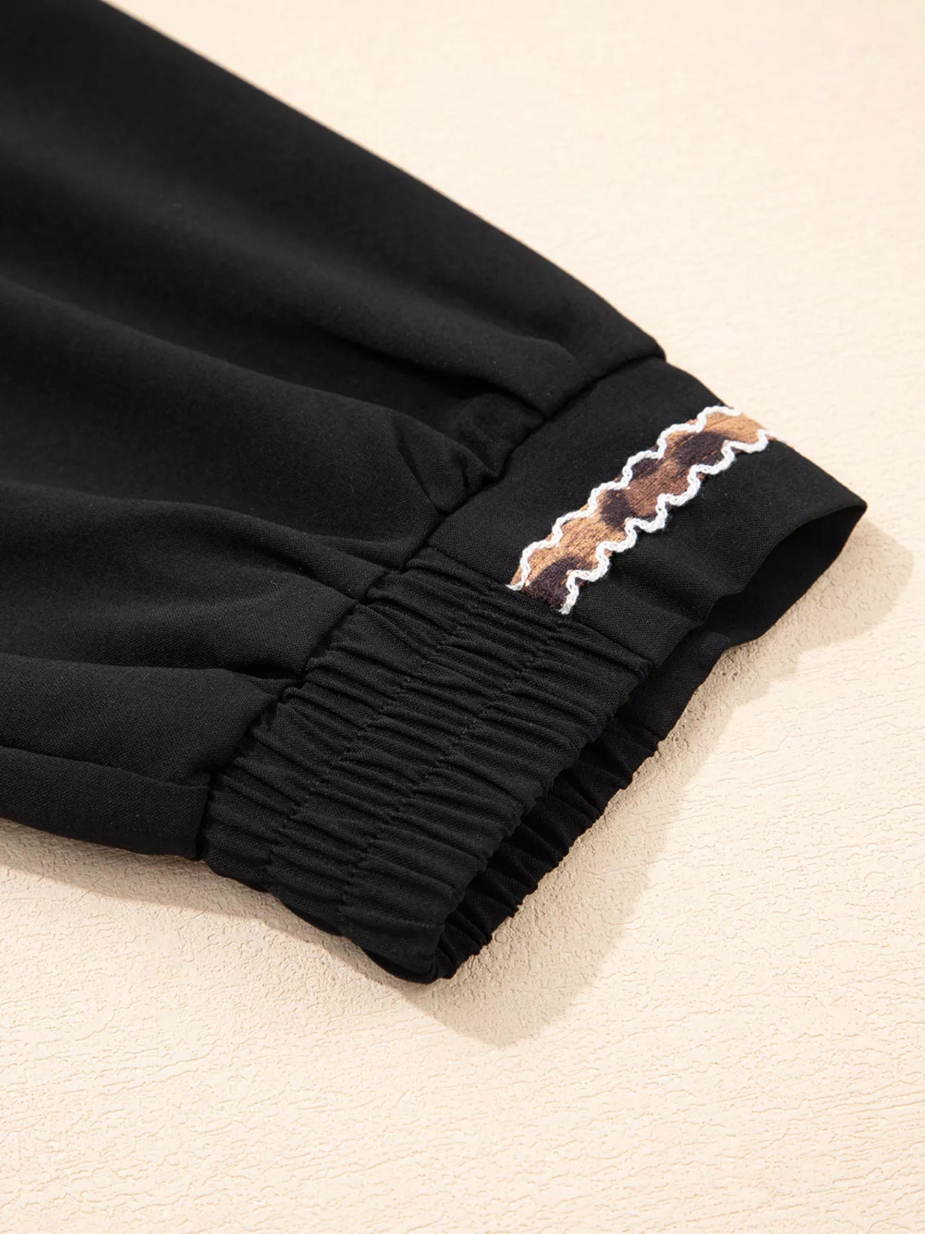 Black pants with decorative trim on a beige background