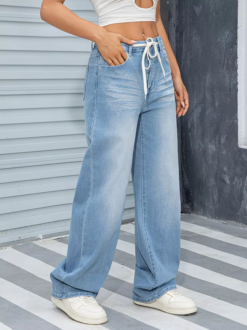 Person wearing light blue jeans and white sneakers on a striped pavement.