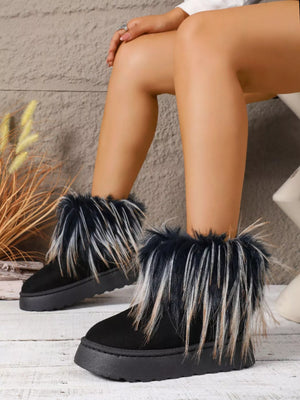 Black suede boots with fur trim worn by a person sitting on a wooden floor.