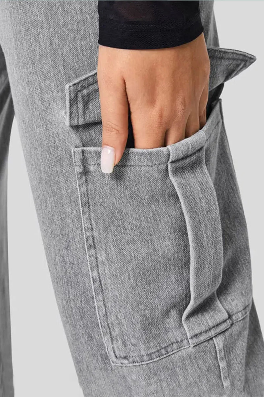 Close-up of a hand with painted nails in the pocket of gray jeans against a neutral background