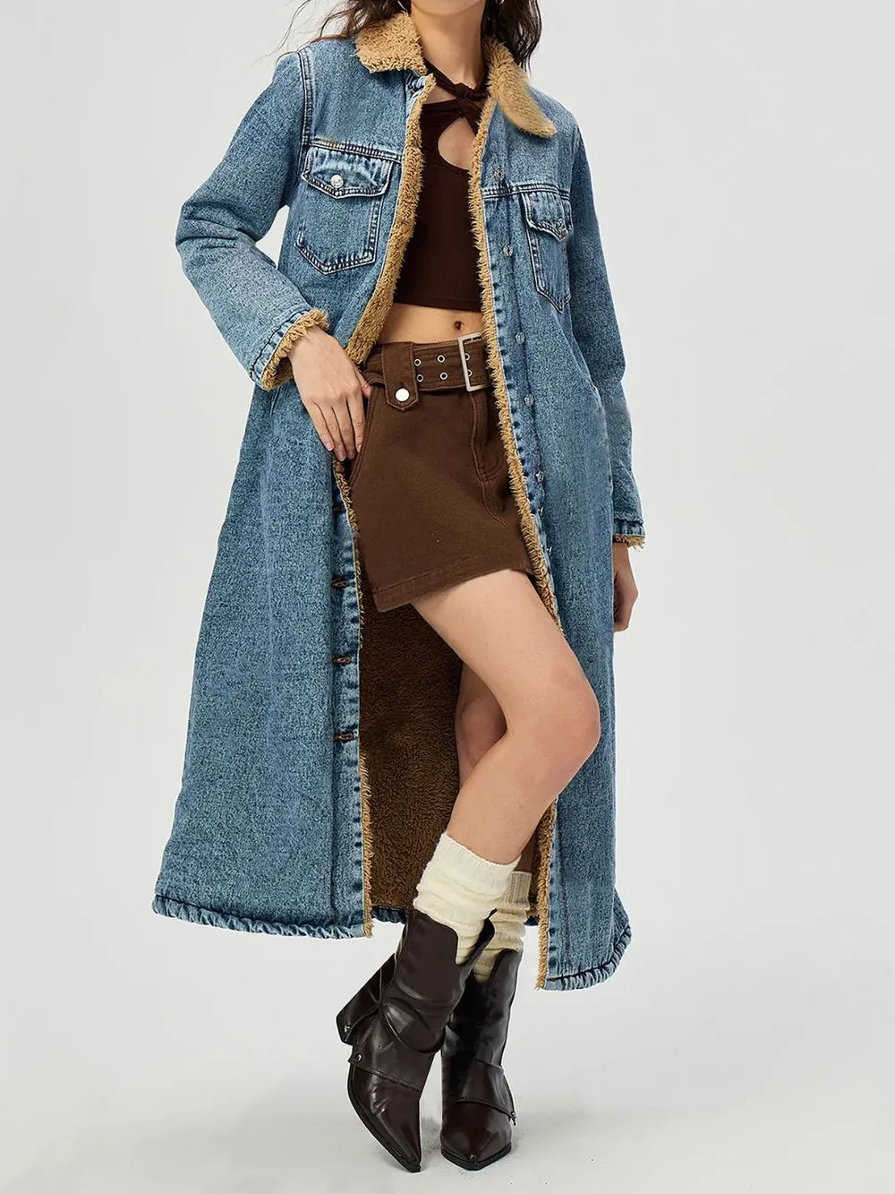 Person wearing a long denim coat with a brown outfit underneath on a white background