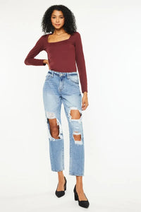 Woman wearing a burgundy long-sleeve top and ripped blue jeans on a white background