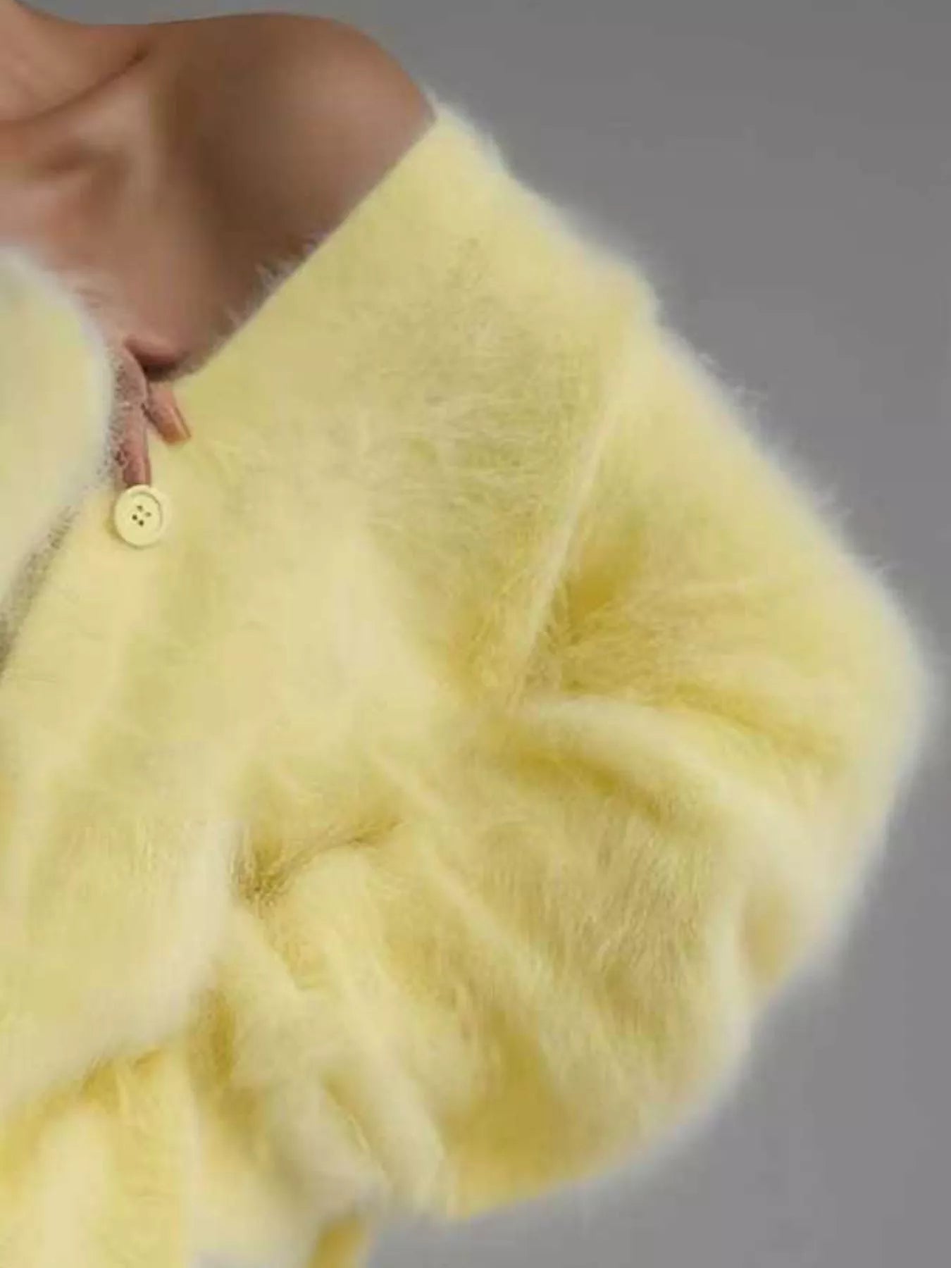 Close-up of a light yellow fluffy garment with a button on a neutral background