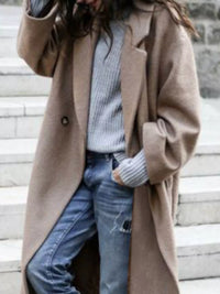Person wearing a beige coat over a light blue sweater and jeans on a stone staircase.