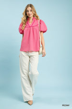 Woman wearing a pink blouse and white pants against a light blue background