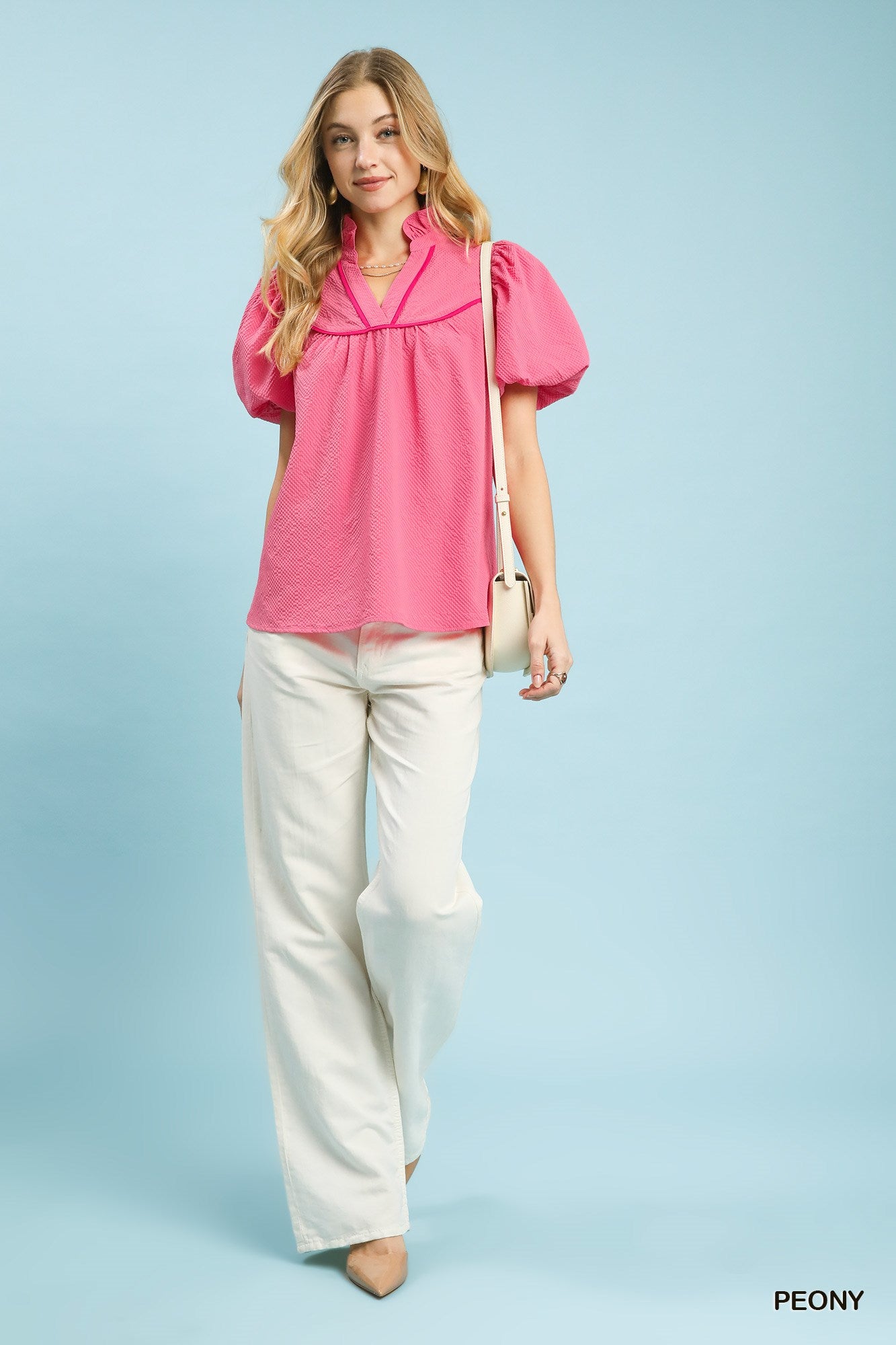 Woman wearing a pink blouse and white pants against a light blue background
