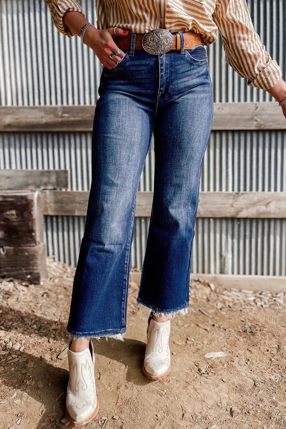 Person wearing blue jeans and a striped shirt with a belt, standing on a dirt ground.