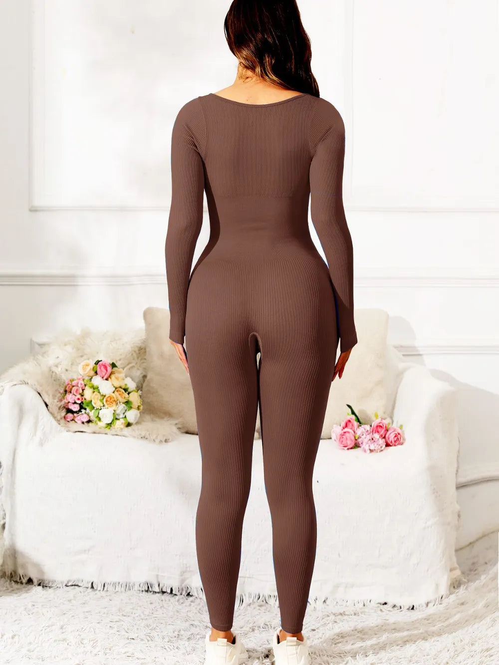Person wearing a brown bodysuit in a minimalistic room with white walls and furniture.