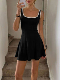 Person wearing a black dress taking a mirror selfie in a neutral setting.