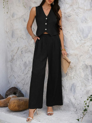 Woman wearing a black sleeveless top and wide-leg pants against a textured wall.