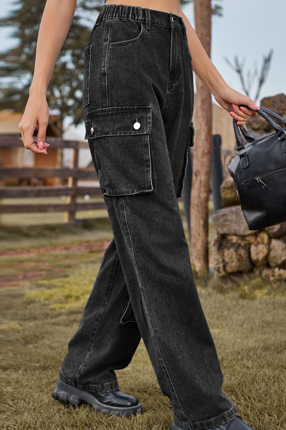 Person wearing black cargo pants holding a black bag outdoors.