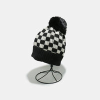 Black and white checkered beanie with a pom-pom on a stand against a light gray background