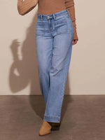 Person wearing light blue jeans and a brown top against a beige background