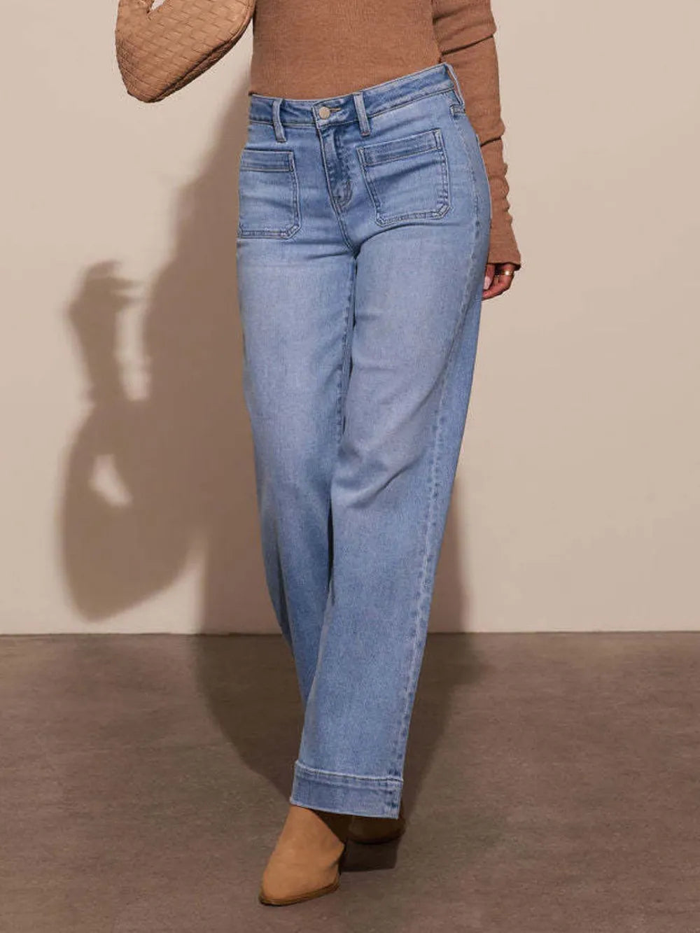 Person wearing light blue jeans and a brown top against a beige background