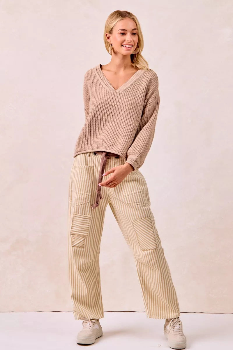 Woman wearing a beige ribbed sweater and pants on a plain background