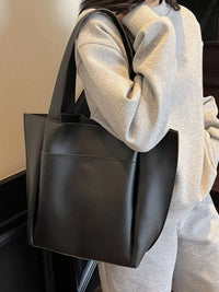 Person holding a black tote bag with a neutral background