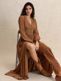 Woman in a long brown dress sitting on a chair against a neutral background