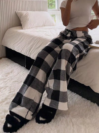Person wearing black and white checkered pants and a white crop top on a bed.