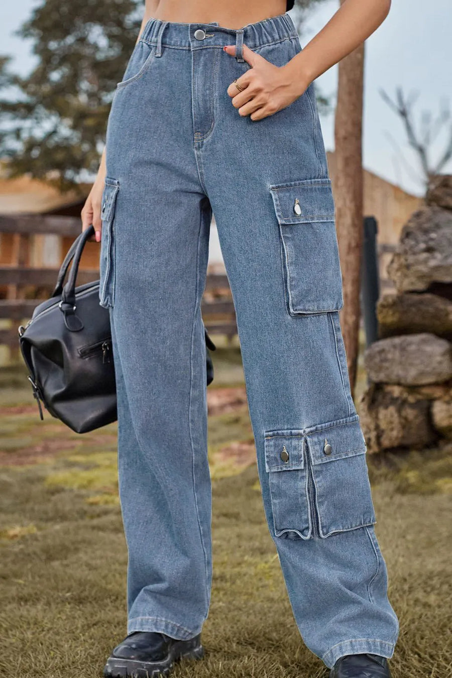 Person wearing blue cargo pants holding a black bag outdoors.