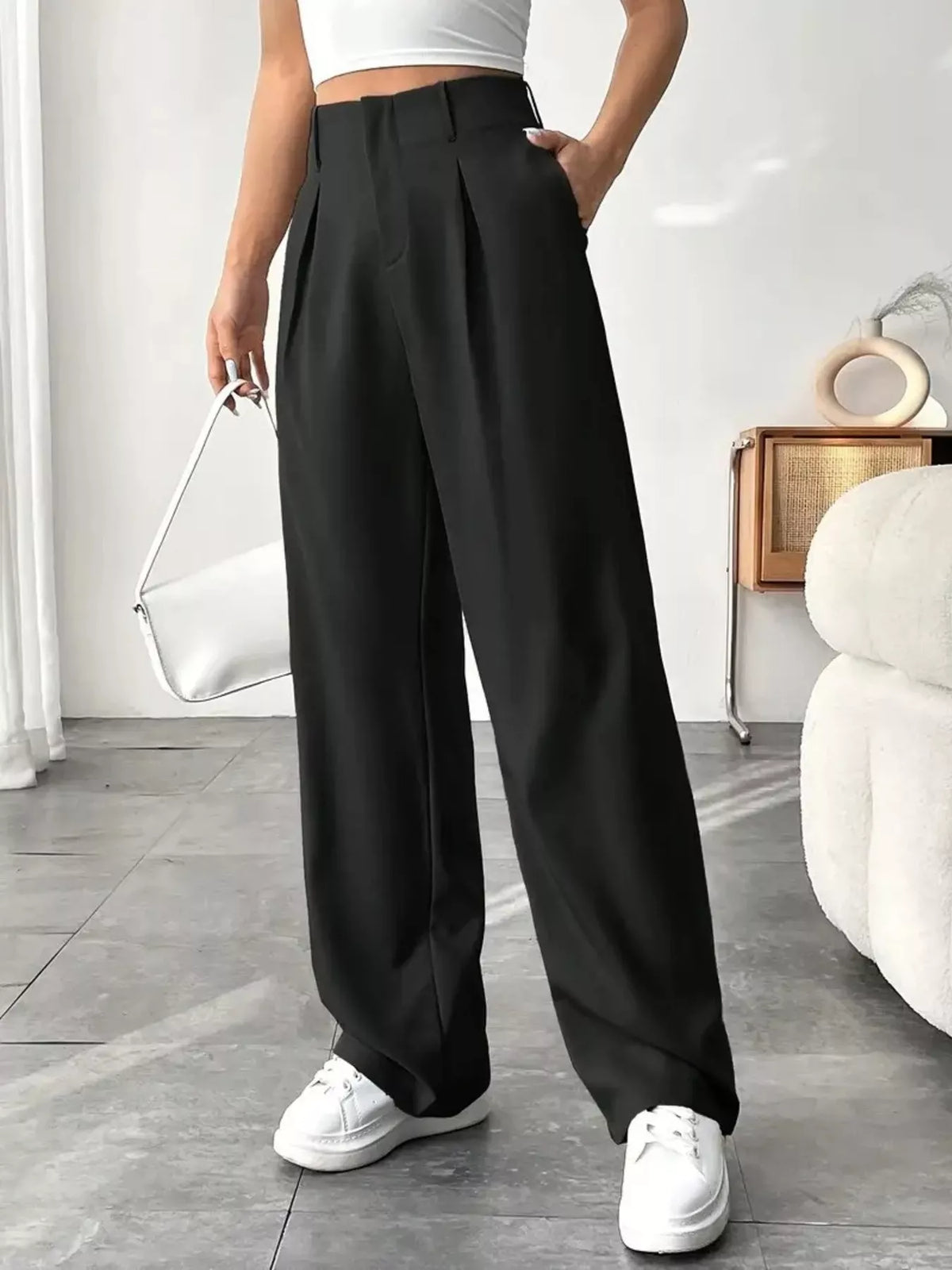 Person wearing black wide-leg pants and white sneakers in a minimalistic room.