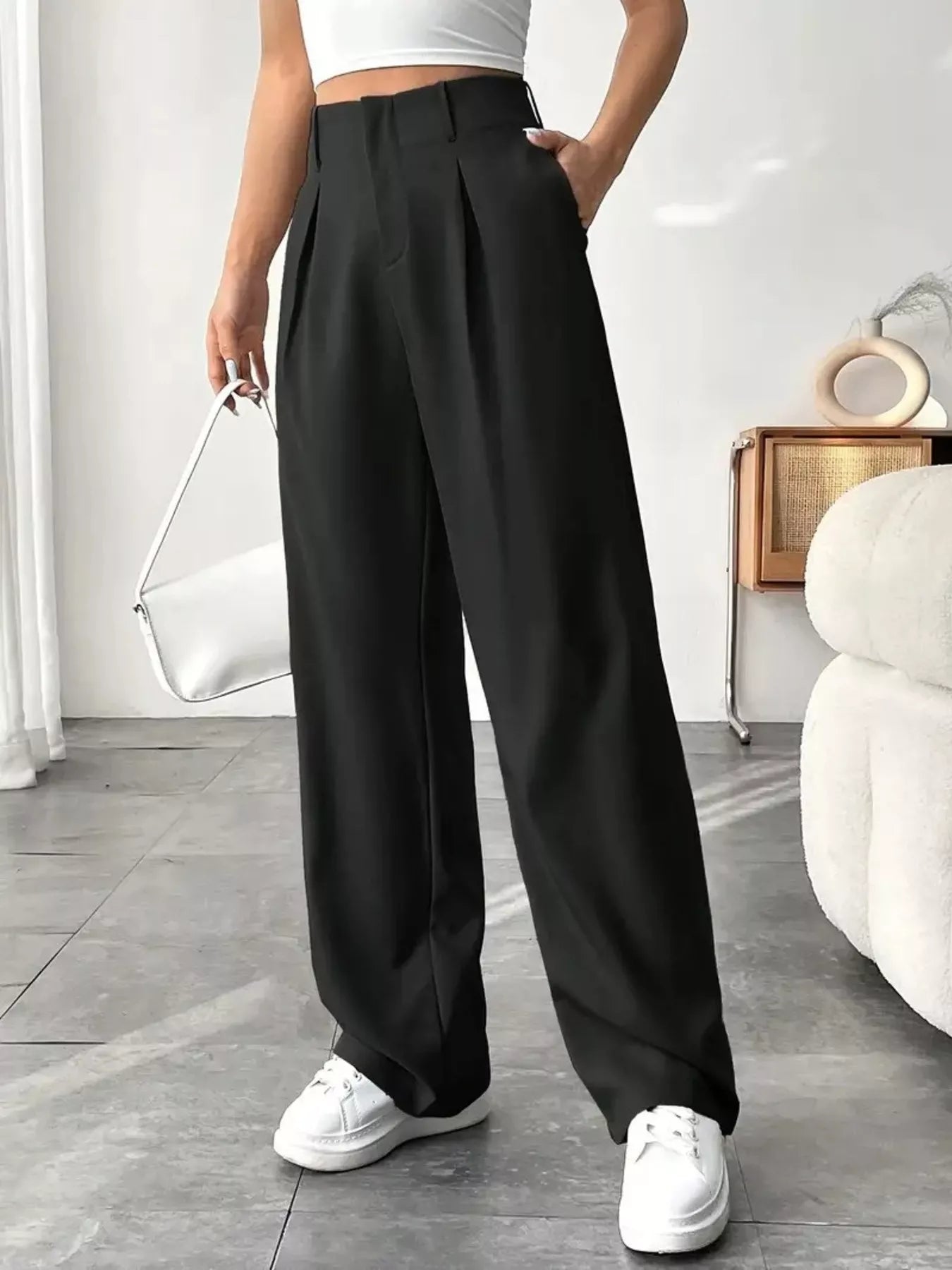 Person wearing black wide-leg pants and white sneakers in a minimalistic room.