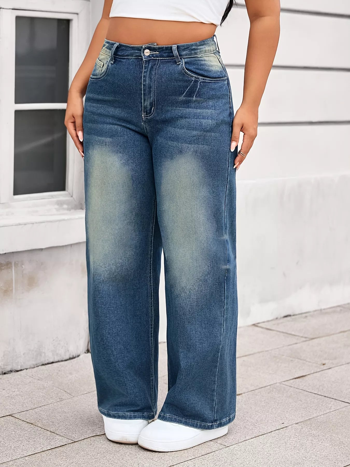 Person wearing blue wide-leg jeans standing on a sidewalk.