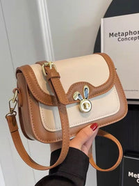 Handbag with brown and beige design held by a hand against a blurred background