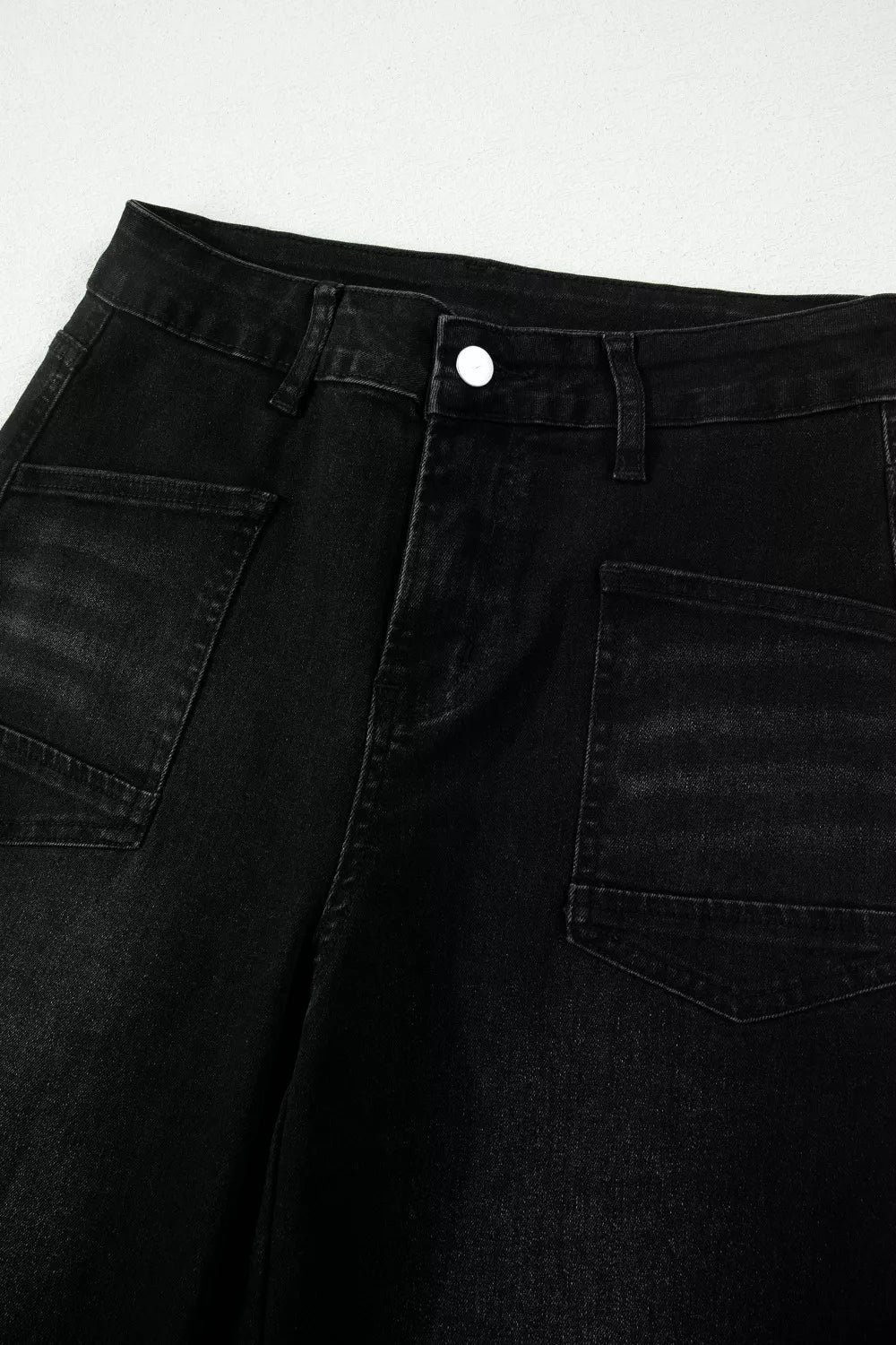 Close-up of black jeans with a button on a light gray background