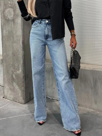 Person wearing blue jeans and a black top, standing against a concrete wall.