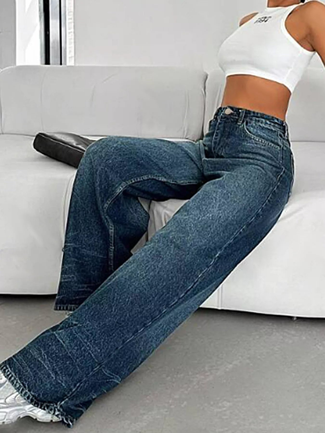 Person wearing blue jeans sitting on a white couch.