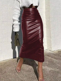 Person wearing a burgundy leather skirt with a white top against a light-colored wall.