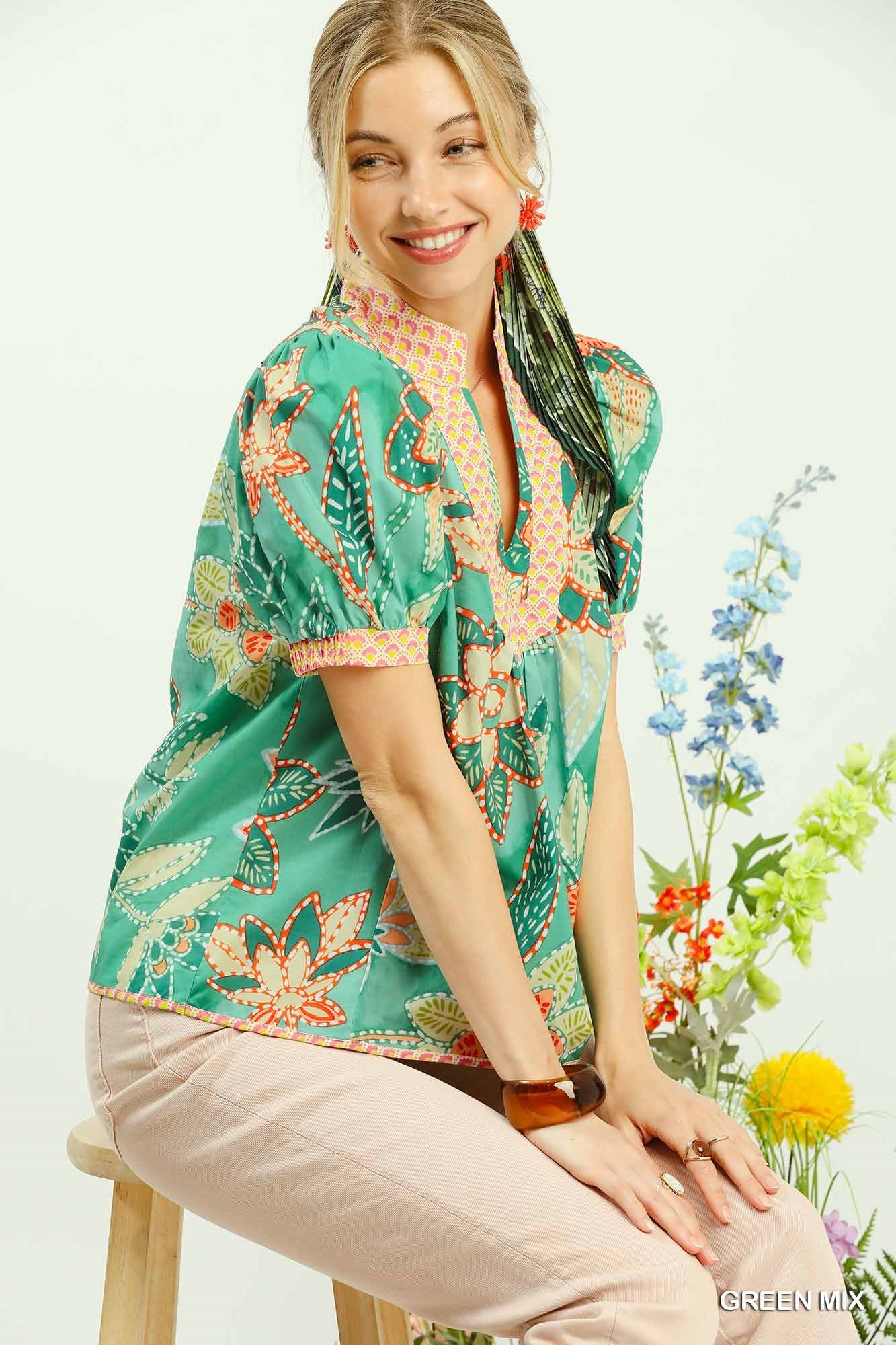 Woman wearing a colorful blouse sitting on a stool with flowers in the background