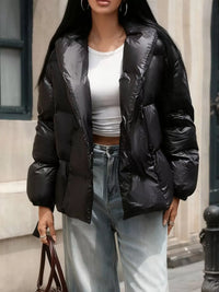 Person wearing a black puffer jacket over a white top and light blue jeans, standing outdoors.