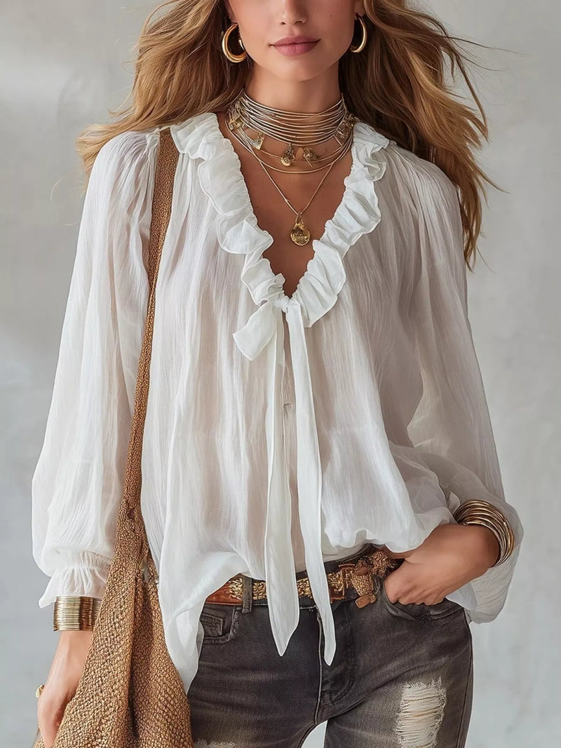 Woman wearing a white blouse with ruffled details and layered necklaces, holding a straw bag.