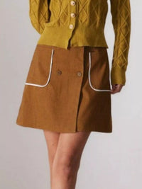 Person wearing a mustard yellow sweater and brown skirt on a plain background