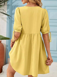 Woman wearing a yellow dress with puff sleeves against a light blue wall.