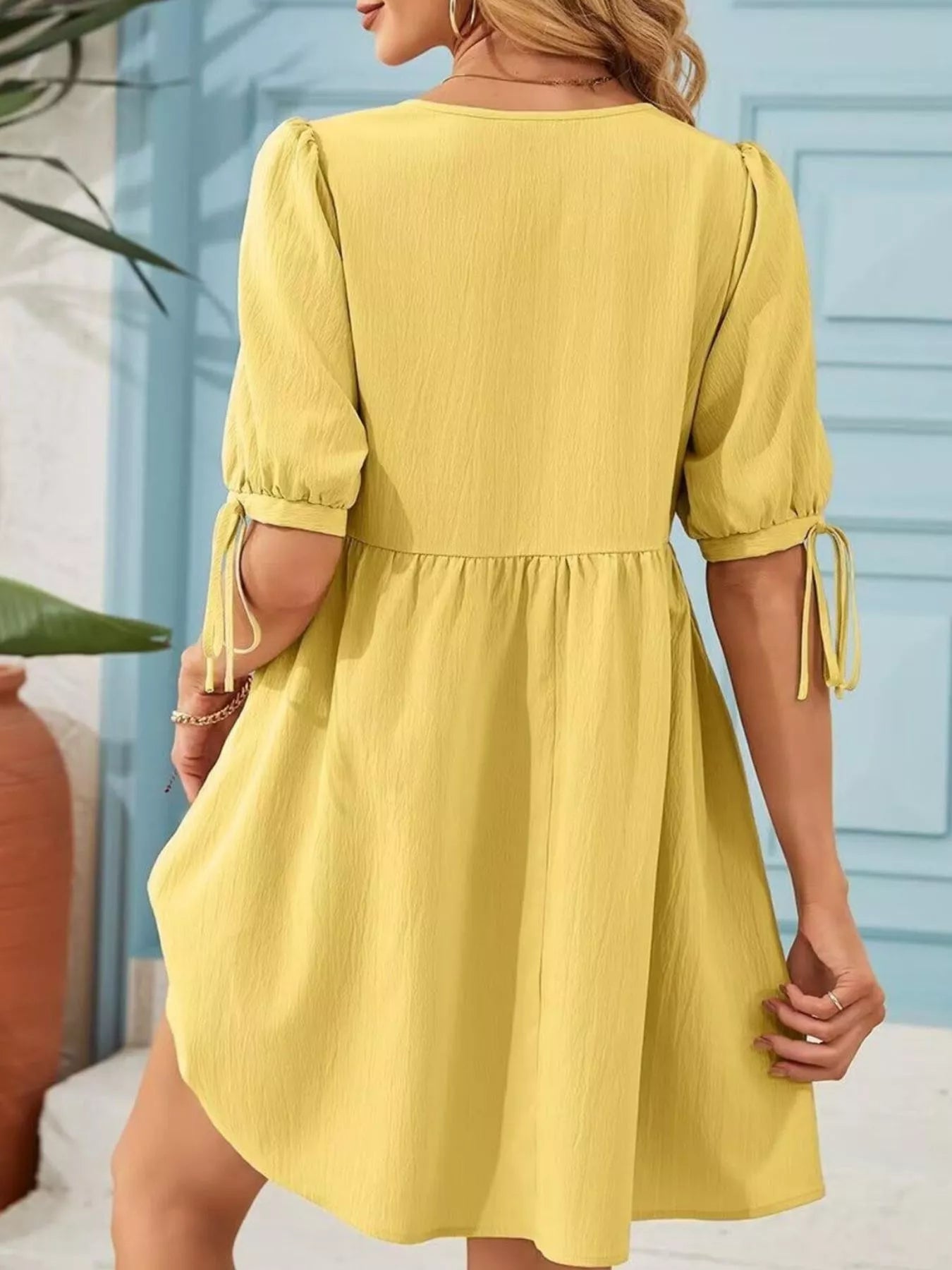 Woman wearing a yellow dress with puff sleeves against a light blue wall.