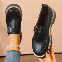 Black leather shoes with a strap held by a person against a beige background