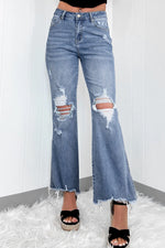 A pair of distressed, raw hem bootcut jeans with a slightly stretchy fabric, displayed on a person against a white background with a furry white surface.