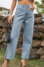 Person wearing light blue jeans standing against a stone wall.
