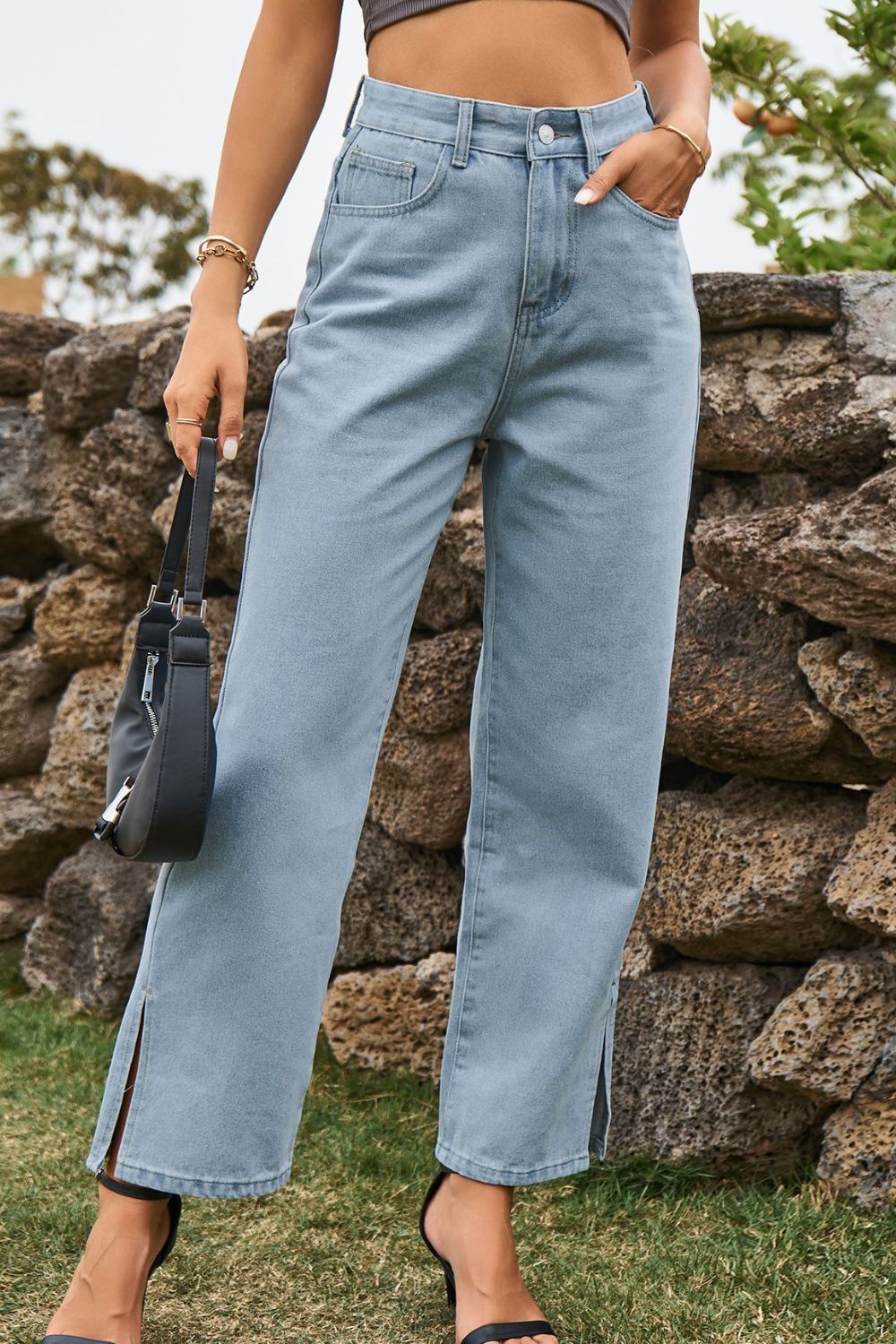 Person wearing light blue jeans standing against a stone wall.